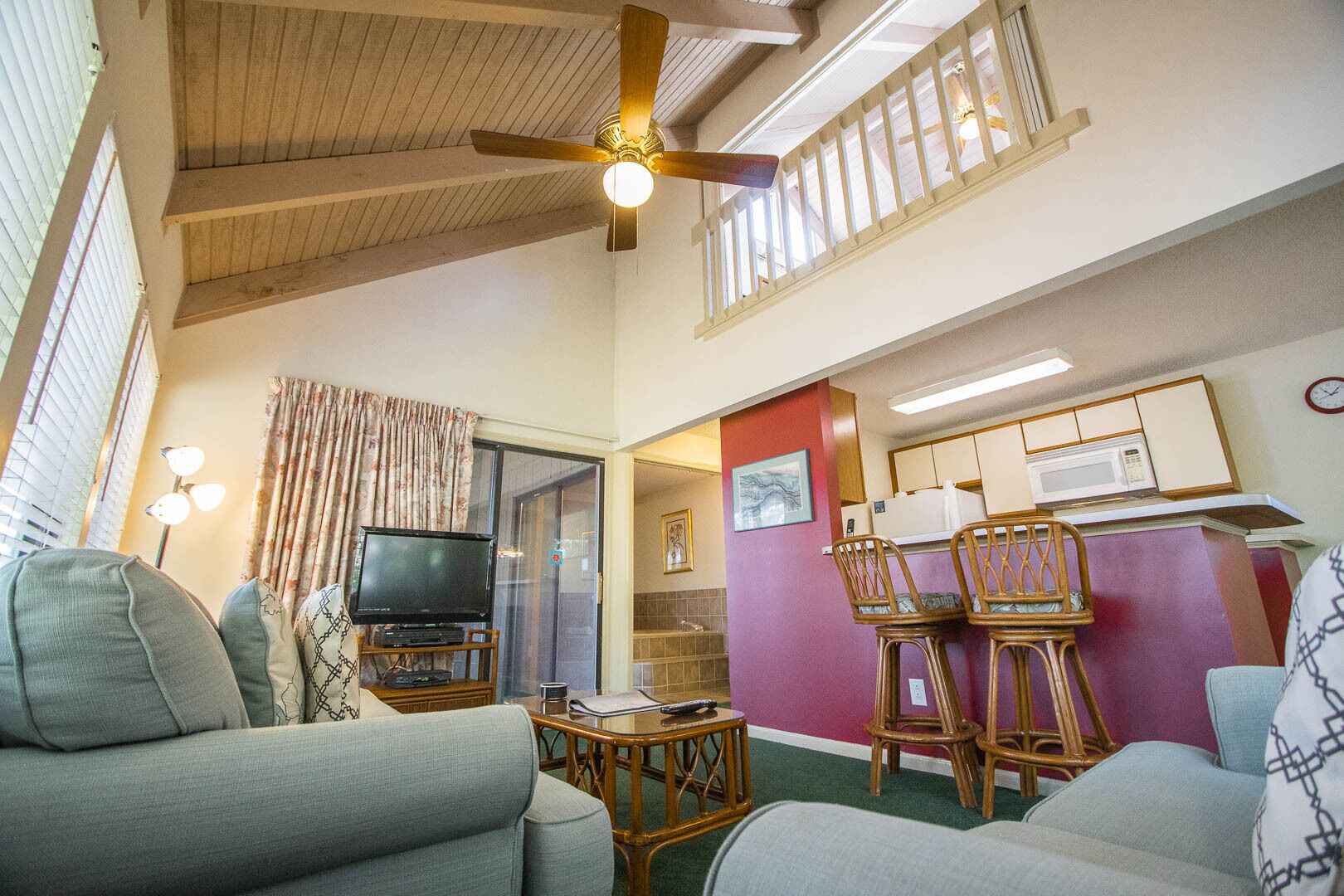 A living room with a television, two sofas, a ceiling fan, and a kitchen area with a microwave.