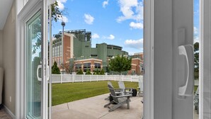 Blick durch eine Glasschiebetür auf eine Terrasse mit Sitzgelegenheiten und ein Gebäude im Hintergrund.