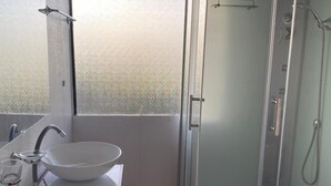 Un baño moderno con ducha de vidrio, un lavamanos blanco y un banco de madera.