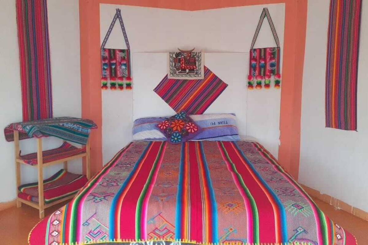 Una habitación con una cama, un estante con mantas dobladas y dos bolsas colgadas en la pared.