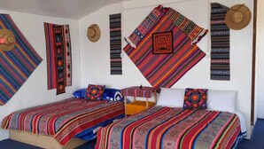 Una habitación con dos camas, cada una con mantas de colores, y una pared decorada con tejidos y sombreros.