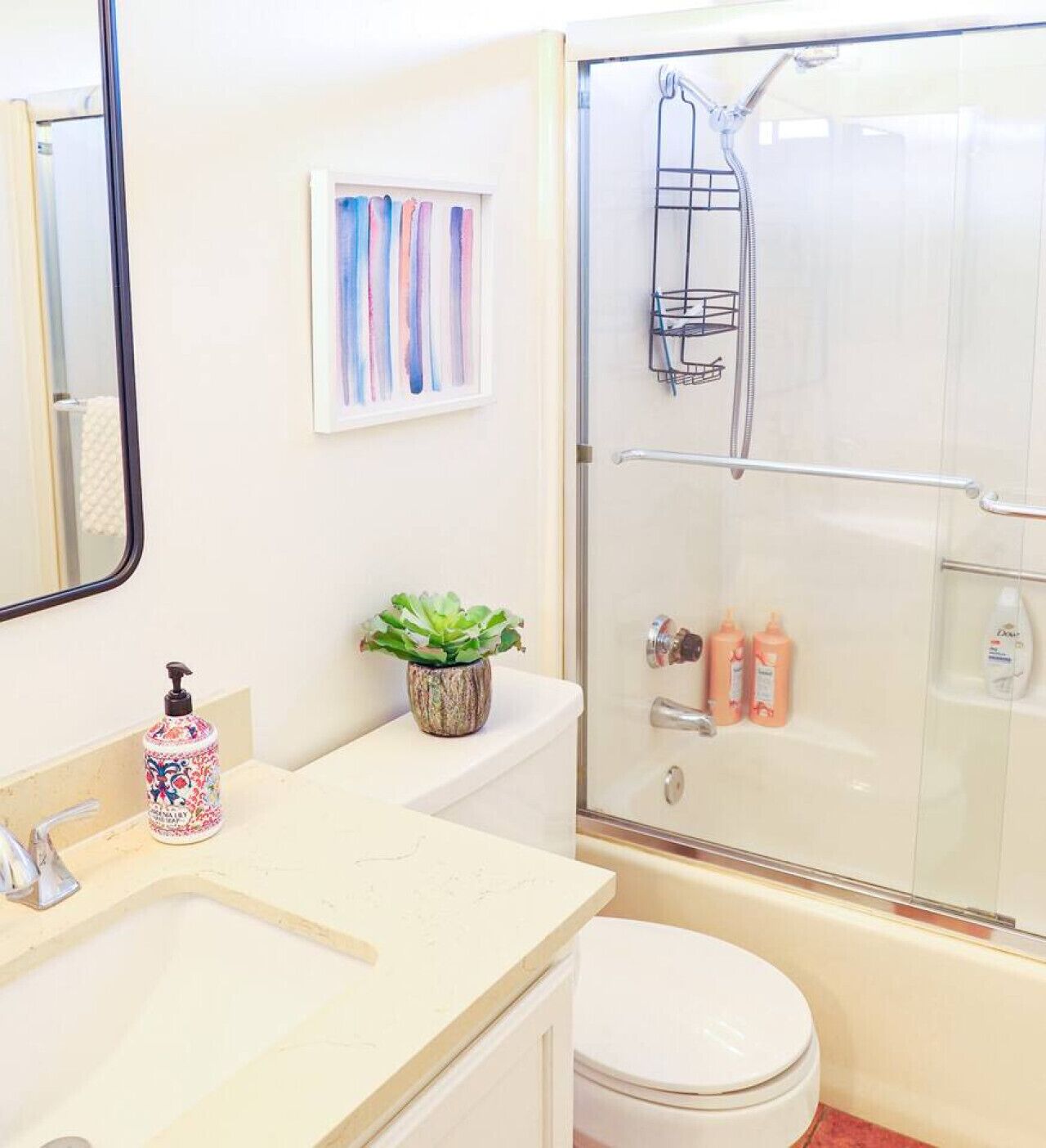 Un bagno con servizi igienici, lavandino e doccia. C'è una pianta sul ripiano e articoli da toilette a parete.