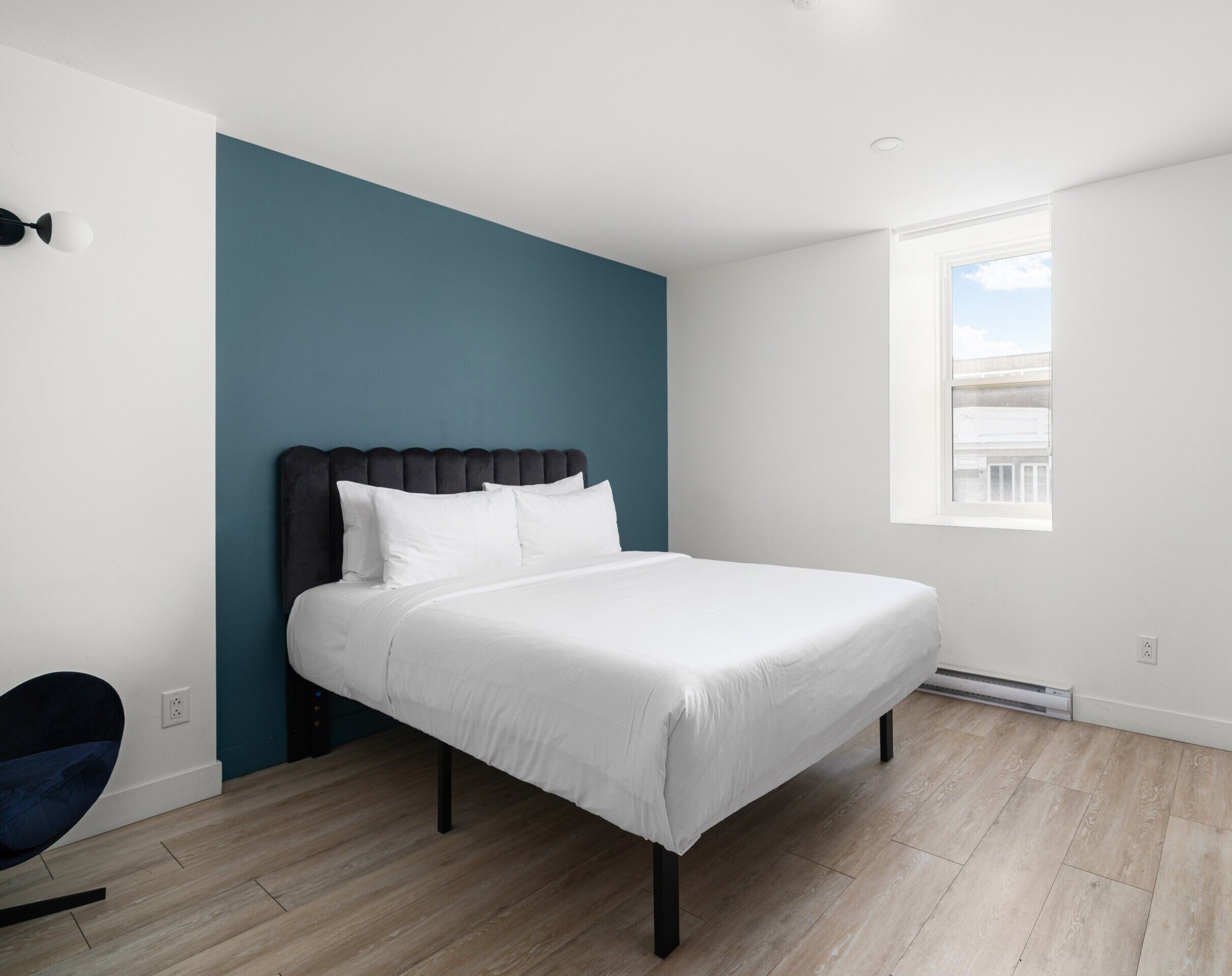 A bedroom with a bed, a window, and a blue accent wall.