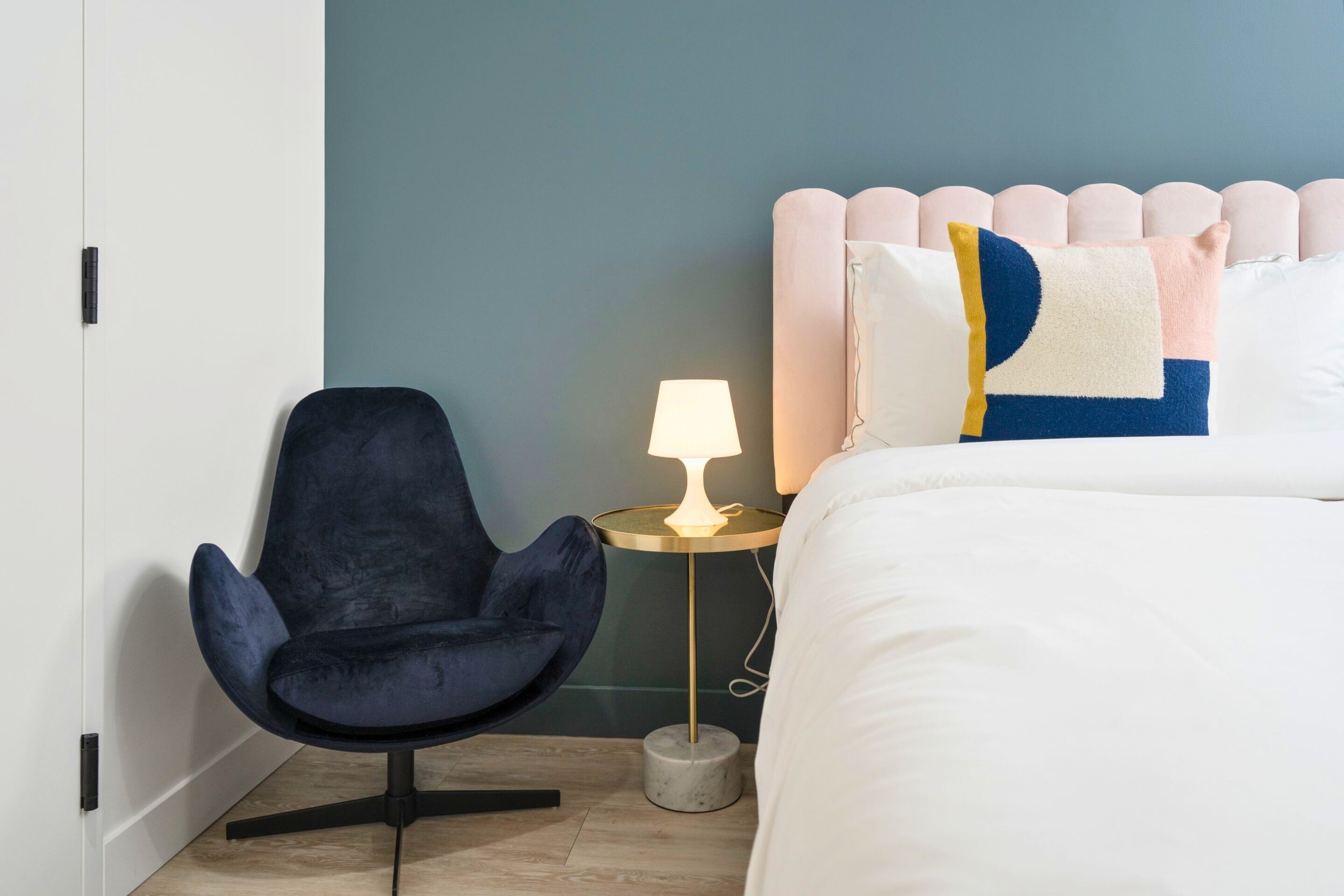 Ein Schlafzimmer mit einem Bett, einem Sessel, einem Nachttisch mit Lampe sowie einer Wand mit einem besonderen Kopfteildesign.