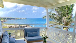 A covered outdoor seating area with a sofa, chairs, and a table, overlooking a beach and ocean. - 5 bedroom relaxation Oceanfront w/ Stunning natural views.  5 bdrms, sleeps 12 (Marley Vale)