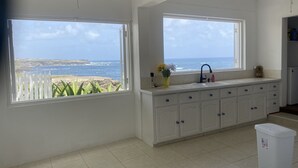 A kitchen with white cabinets, a sink, and a trash bin. There are two windows offering a view of the ocean. - 5 bedroom relaxation Oceanfront w/ Stunning natural views.  5 bdrms, sleeps 12 (Marley Vale)