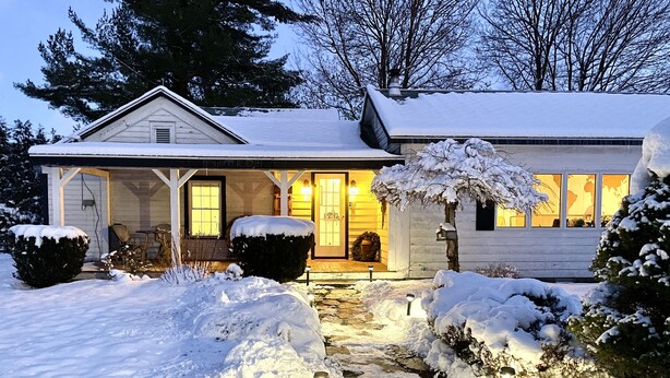Een huis bedekt met sneeuw, met een veranda, een pad naar de ingang en een klein tuintje.