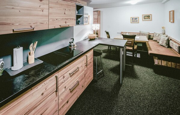 Een moderne keuken met houten kastjes, een zwart aanrecht en een eethoek met een tafel en stoelen.