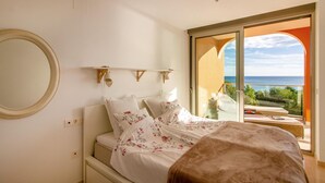 A bedroom with a bed, a large mirror, and a view of the sea through a glass door.