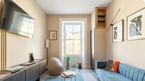 Ein modernes Wohnzimmer mit einer Couch, einem an der Wand montierten Fernseher, einem großen Fenster und einem kleinen Tisch mit einer Pflanze.