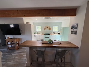 A kitchen with a wooden island, two chairs, a TV, and a dining table.