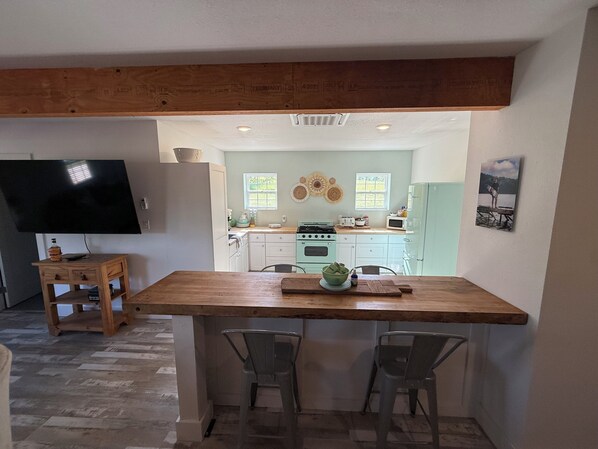 A kitchen with a wooden island, two chairs, a TV, and a dining table.