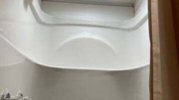 Une baignoire blanche au design incurvé, avec un robinet apparent et une pomme de douche.