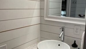 A bathroom with white tiled walls, a white sink, and a mirror above the sink. - House - The Fais Do Do (Hattiesburg)