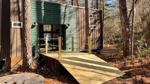 A rustic cabin with a wooden deck and a ramp leading to the entrance. - House - The Fais Do Do (Hattiesburg)