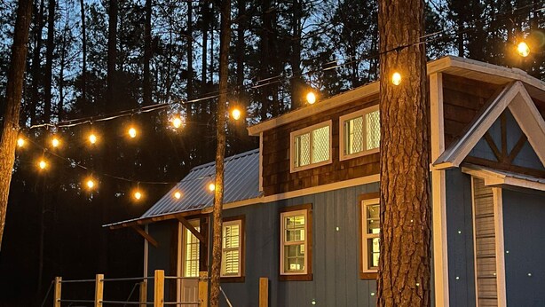 Eine Holzhütte mit einer Holzterrasse, mehreren Fenstern und Lichterketten.