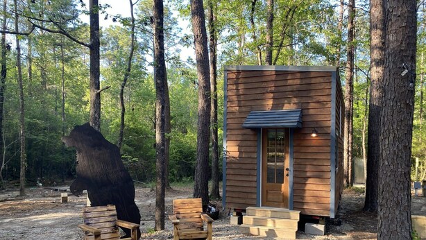 A cabin with a wooden exterior, a door, and a small porch area with two wooden benches. - Tiny House - Shangri La (Hattiesburg)