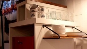 A kitchen with a white countertop, a red cabinet, and a hanging rack with plates and glasses. - Tiny House - Shangri La (Hattiesburg)