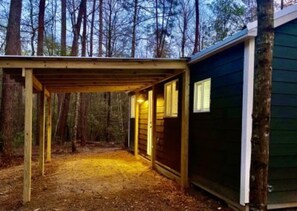 A wooden structure with a covered entrance, surrounded by trees. - Tiny House - The Roadhouse (Hattiesburg)