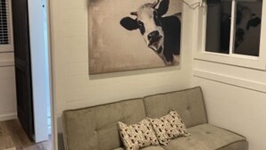 En stue med en sofa, et maleri af en ko, et vindue og en dør.