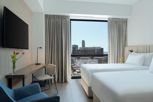 A hotel room with a bed, a desk, a chair, a TV, and a view of the cityscape. - NH Iquique Pacifico (Iquique)