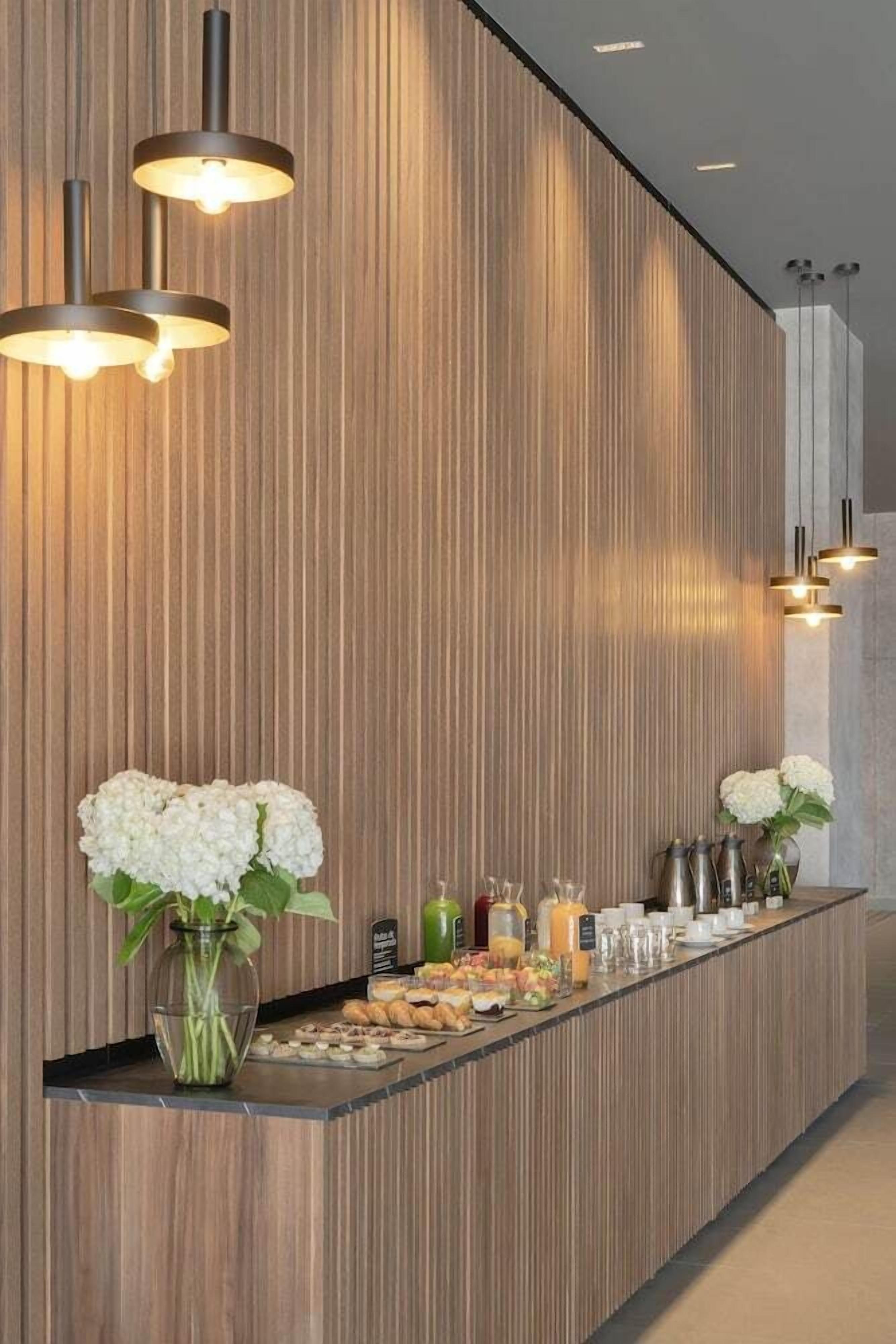 Una moderna zona de recepción con un panel de madera, una larga barra con comida y bebidas, e iluminación colgante.