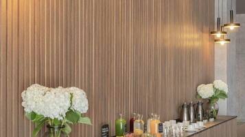 Una moderna zona de recepción con un panel de madera, una larga barra con comida y bebidas, e iluminación colgante.