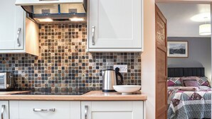 Una cocina con armarios blancos, salpicadero de azulejos y un hervidor sobre la encimera.