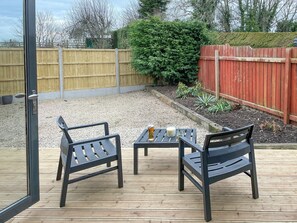 An outdoor patio with two chairs and a table, a wooden deck, a gravel area, and a red fence. - Woodside Retreat, Number 37 (Newbold Coleorton)