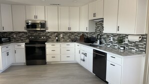 A modern kitchen with white cabinets, a stainless steel refrigerator, a microwave, a stove, and a dishwasher.