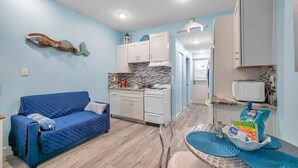 Een compacte woonruimte met een blauwe bank, kitchenette en een eethoek met een tafel en stoelen.