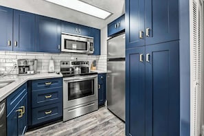 A modern kitchen with blue cabinets, stainless steel appliances, and a tiled backsplash.