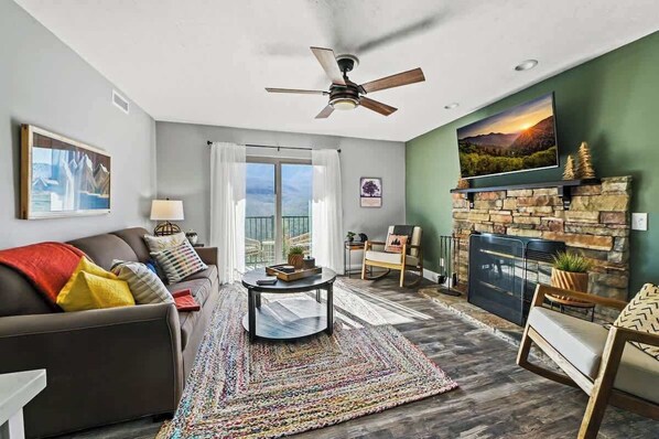 A living room with a sofa, coffee table, fireplace, and a television mounted above it.