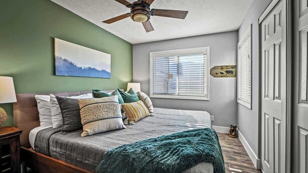 Quarto com cama, ventoinha no teto, janela com persianas e quadro na parede.