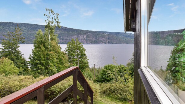Une terrasse en bois offrant une vue sur un lac et des collines boisées.