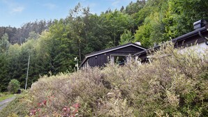 Une cabane entourée d’une forêt dense, sous un ciel dégagé.