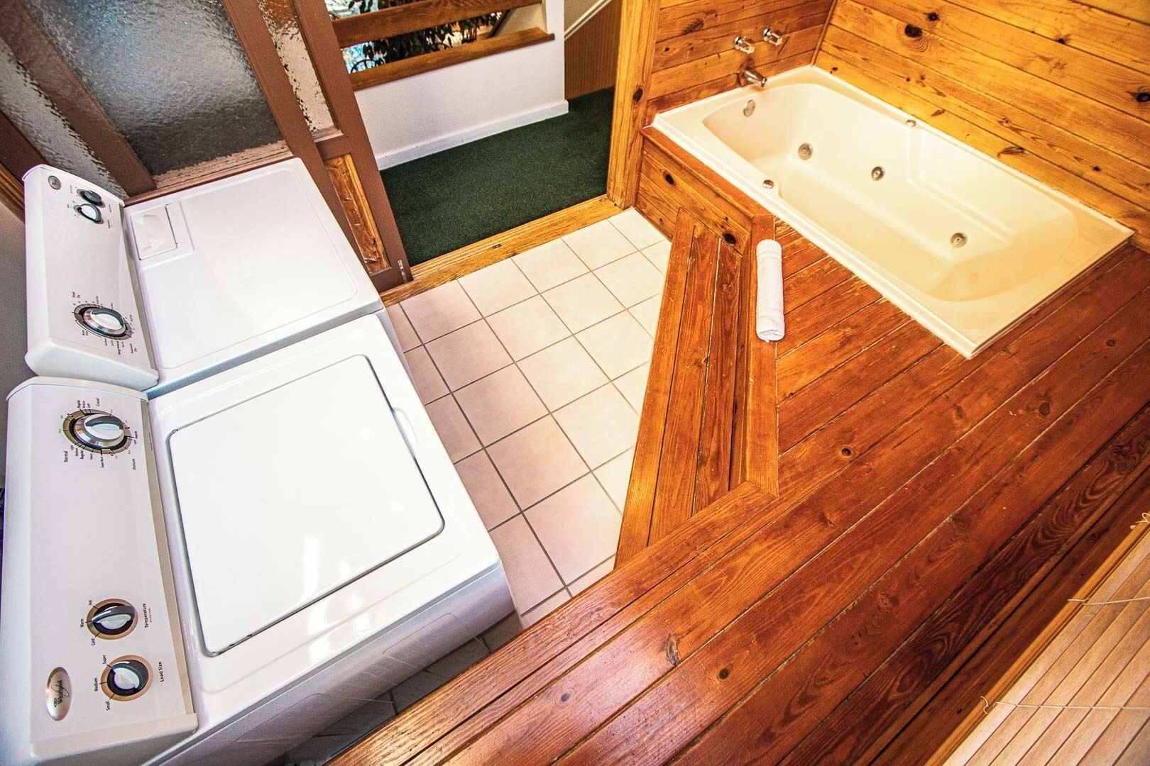 Ein kleines Badezimmer mit Holzboden, einer weißen Badewanne und einer Waschmaschine.