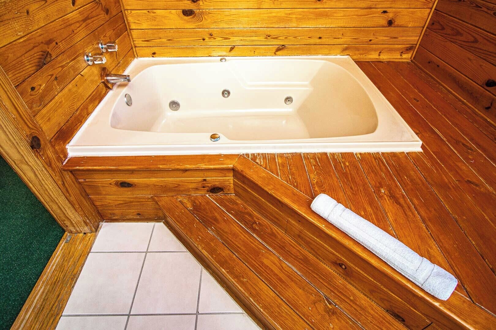 A wooden cabin with a white bathtub, wooden flooring, and a towel on the floor.