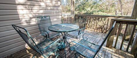 A wooden deck with a metal table and chairs, surrounded by trees.