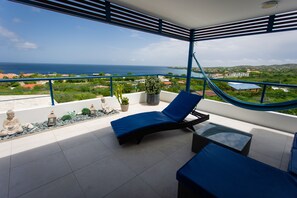 Een balkon met een blauwe loungestoel, een tafeltje en een hangmat.
