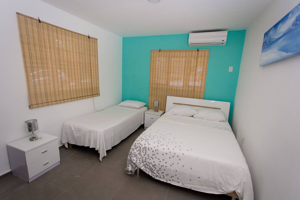 A bedroom with two single beds, a nightstand, a drawer unit, and an air conditioning unit on the wall.