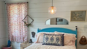 Een slaapkamer met een bed, een hanglamp, een spiegel en een raam met gordijnen.