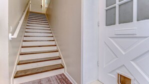 Una escalera de madera que sube hacia una puerta blanca con un ventanal.