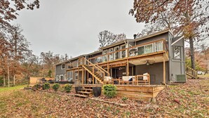 A two-story house with a wooden deck, outdoor seating, and a staircase leading to the upper level. - Lakefront Rogers Getaway w/ Hot Tub & Deck! (Rogers)