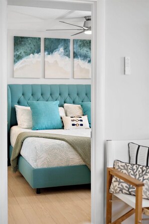 A bedroom with a teal upholstered bed, multiple pillows, a ceiling fan, and three abstract wall art pieces. - OCEAN FRONT Gem w/Pools, Movie Theater, Game Room, SunsetCove at SeaWatch (Ocean City)