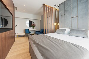 Una camera d'albergo moderna con un letto grande, una scrivania con una sedia, uno specchio rotondo e un pannello decorativo a parete.