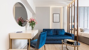 A modern living room with a blue sofa, a round mirror, a small table with a bowl, and a desk with a vase of flowers. - Caldo Luxury Rooms (Split)