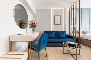 Un soggiorno moderno con un divano blu, uno specchio rotondo, un tavolino con una ciotola e una scrivania con un vaso di fiori.