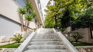 A set of concrete stairs leading up to a building with a stone wall on one side and a metal fence on the other. - Caldo Luxury Rooms (Split)