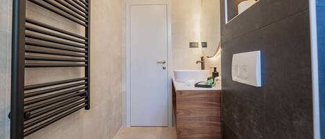 Un baño moderno con toallero, una puerta blanca, lavamanos con artículos de aseo y un espejo.